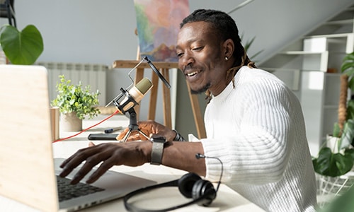 Man talking into a podcast microphone attached to a laptop.